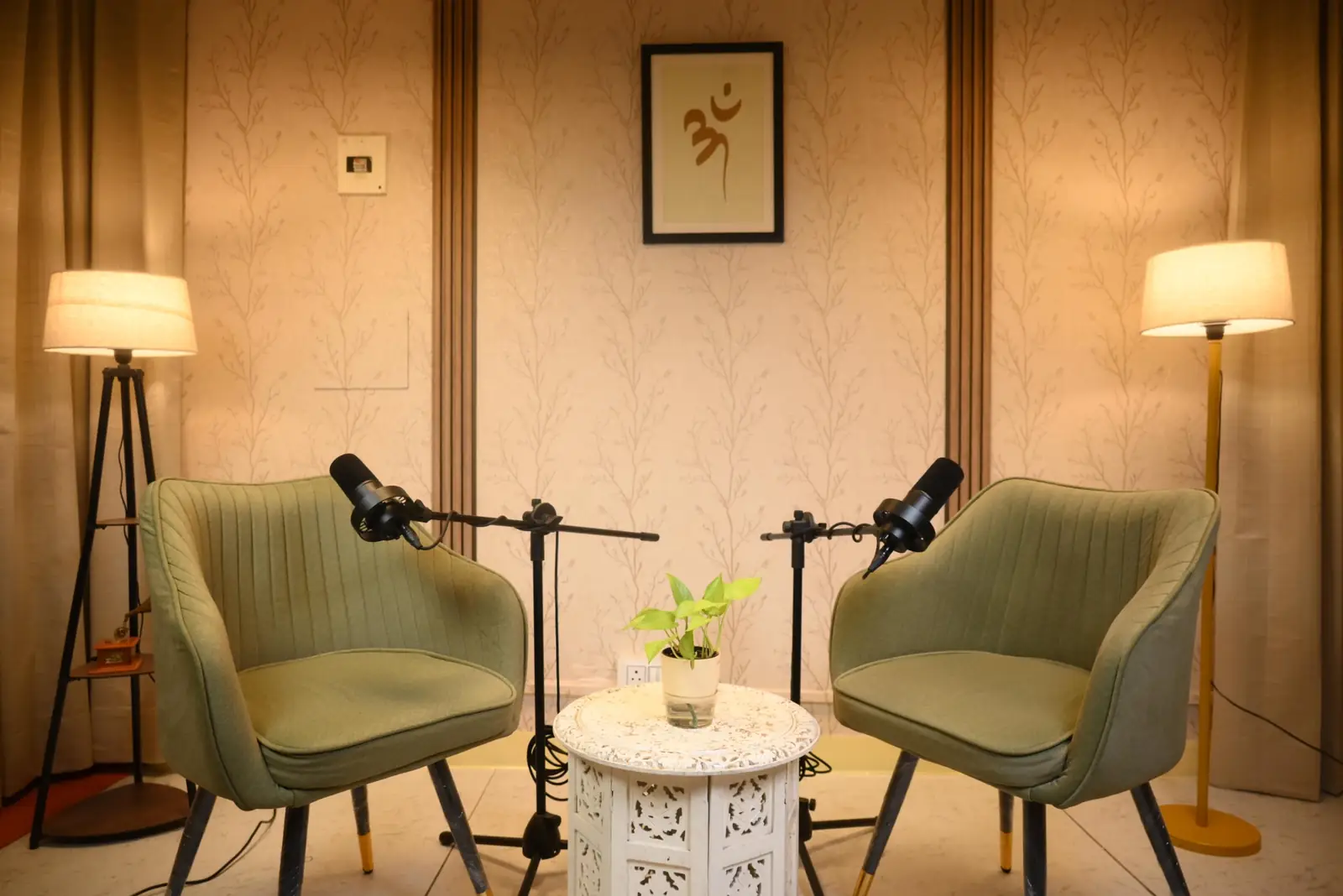 Bintin Media podcast studio in Delhi with two olive lounge chairs, boom microphones, warm floor lamps and Om artwork