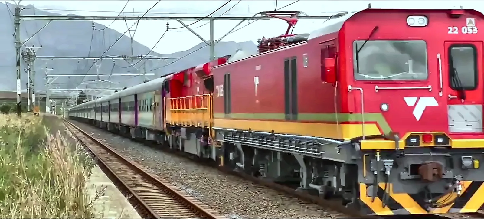 Red electric locomotive hauling a passenger train on an overseas railway line, from the IRCON International corporate film