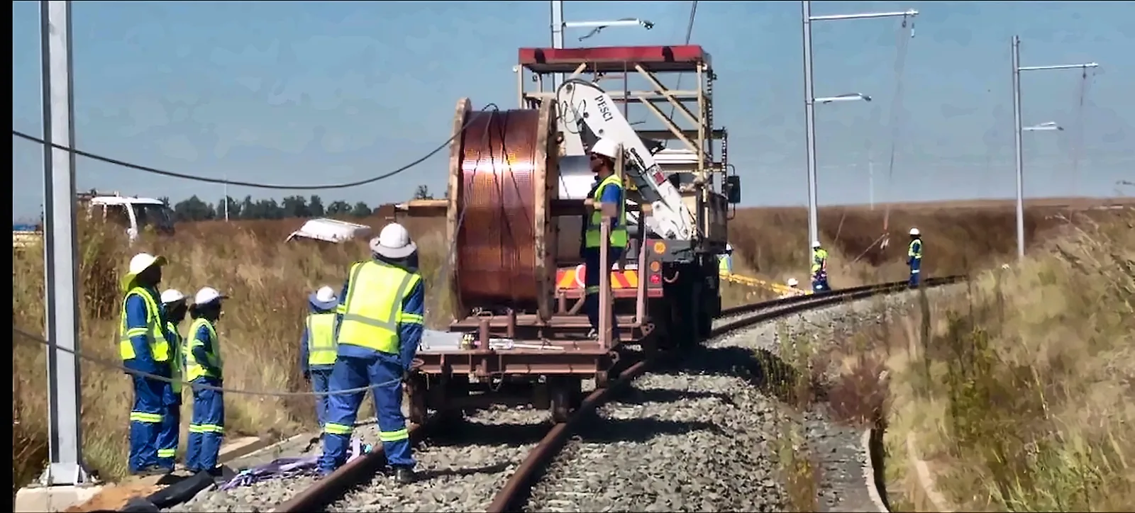Railway electrification team in safety vests unrolling overhead contact wire from a cable drum, from the IRCON corporate film