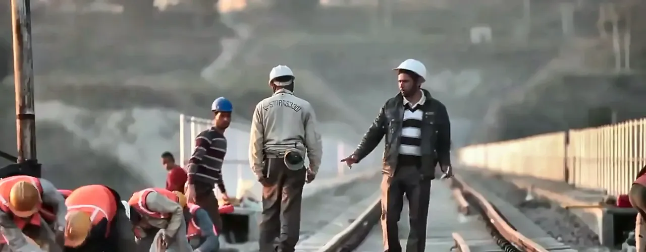 Railway track workers and site supervisors in hard hats on a bridge deck, from the IRCON International film