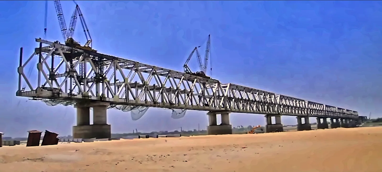 Steel truss bridge girders being launched across a wide river, from the IRCON International corporate film