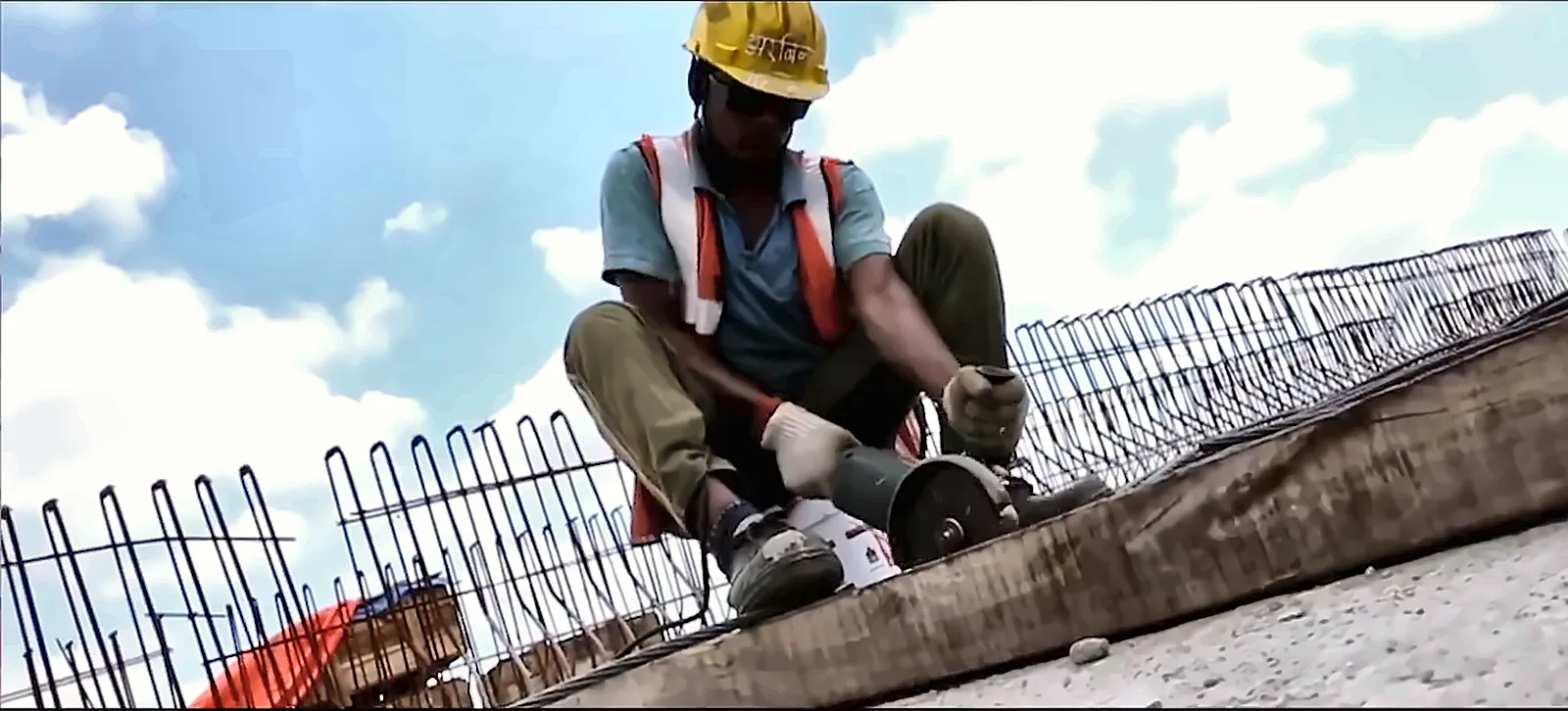 Worker in a yellow helmet cutting reinforcement bars on a bridge deck, from the IRCON International corporate film