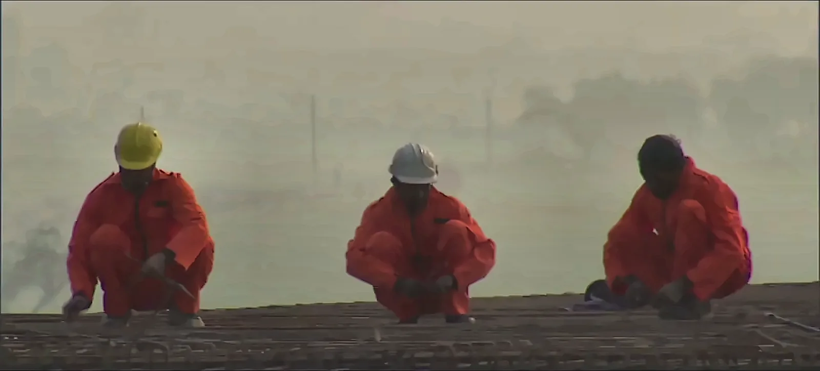 Three workers in red coveralls and helmets at a railway construction site, from the IRCON International corporate film