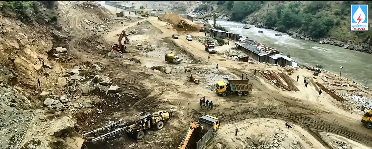 Aerial drone view of an SJVN hydro project construction site with excavators and dumpers beside the river