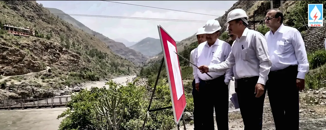 SJVN officials in hard hats reviewing a project plan during a site inspection in a mountain valley