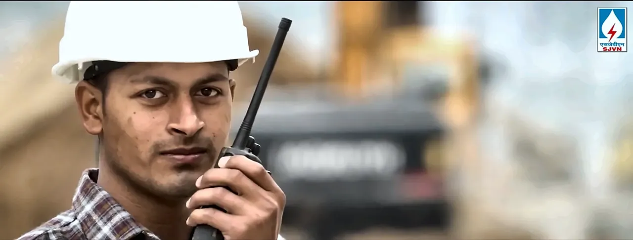 Close-up of an engineer in a white hard hat speaking on a walkie-talkie at an SJVN project site