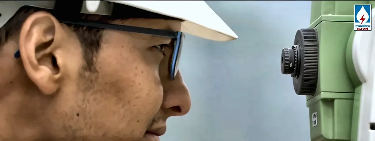 Close-up of a surveyor in a hard hat looking through a total station at an SJVN project